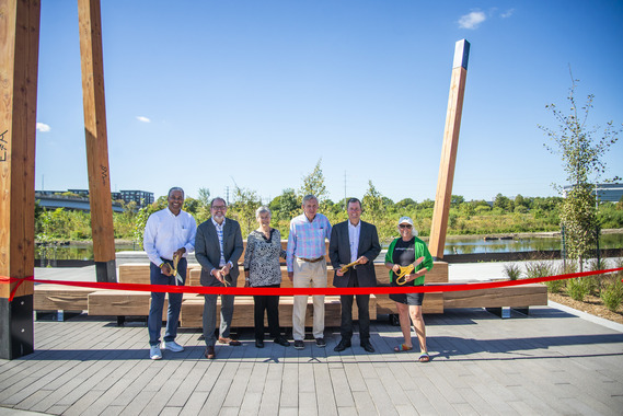 Six people stand in front of a red ribbon with gold scissors at the Graco Park Ribbon Cutting