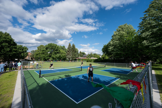 A wide-angle photo shows four people playing pickleball on two new outdoor courts at Dickman Park