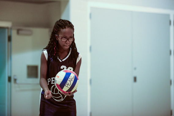 A girl in a blue uniform holds a volleyball as she prepares to serve