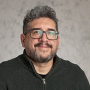Jason Garcia Headshot. Person with glasses, a beard and dark gray sweater in front of a gray background