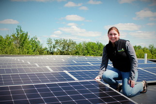 GreenCorps member in front of solar roof panels