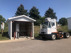 An electric truck parked next to a shed with charging station