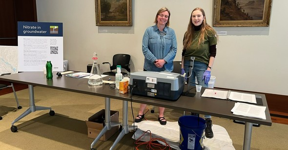 Megan at a testing table next to a nitrate in groundwater display