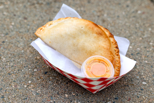 Close up photo of an empanada with a small container of orange-colored sauce