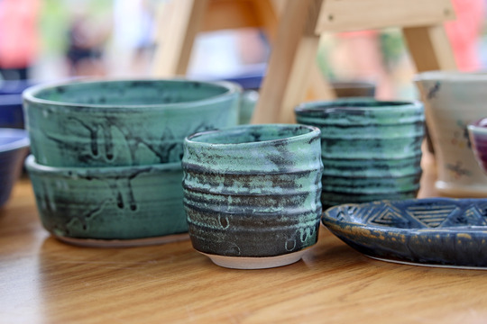 Photo of two blue-green pottery bowls stacked on a table with two pottery cups in front.