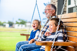 A grandpa and 2 grandchildren smiling on porch swing