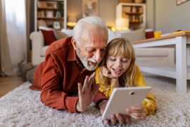 grandpa and granddaughter on tablet laying on floor