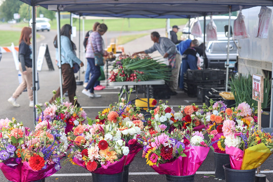Photo of bright flower bouquets in the foreground and a table of vegetables in the background.