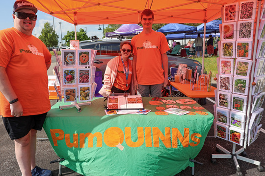 Photo of three young adults smiling and standing by a table with racks of photo greeting cards on display.