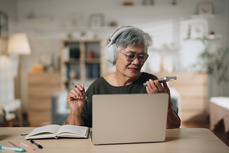 Woman using laptop computer with notebook and wearing headphones