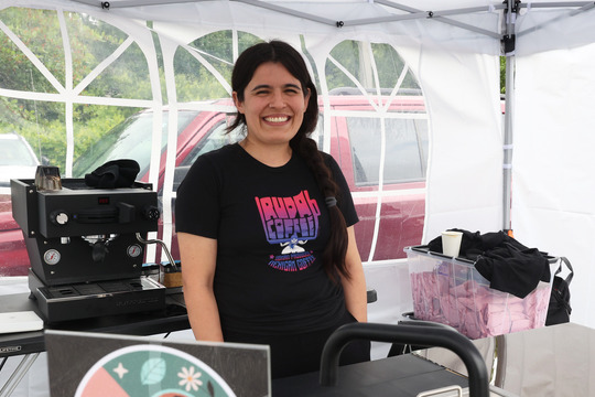 Photo of woman in a white tent wearing a colorful shirt that says Ruda Coffee