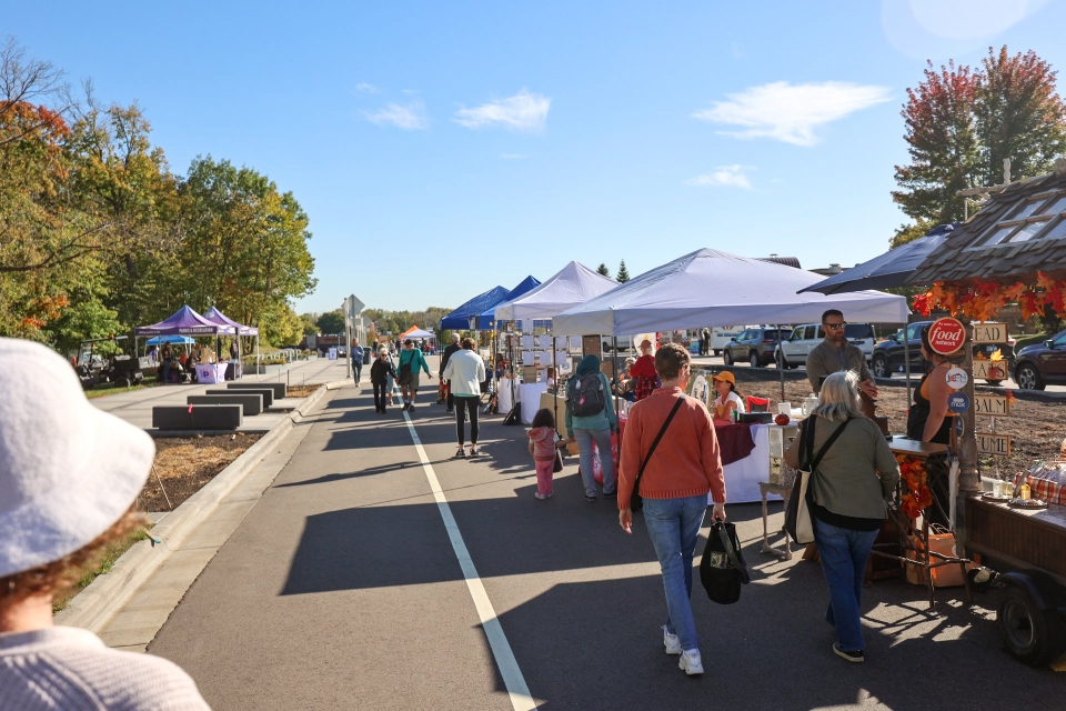 Image of farmers market vendors lined up on a street with shoppers walking by.