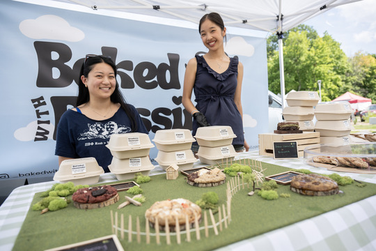 Photo of two young women smiling behind a table of creatively displayed baked cookies.