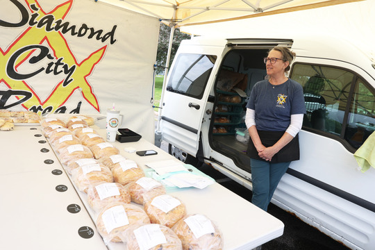 Photo of a woman standing behind a table with loaves of bread on display