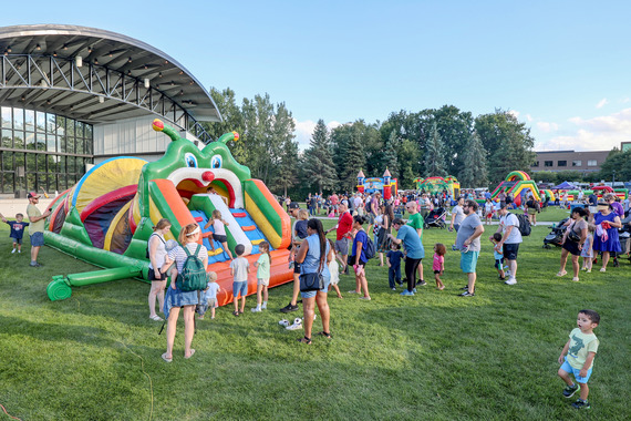 Photo of a large crowd of adults and kids in a park near a large colorful inflatable play structure.