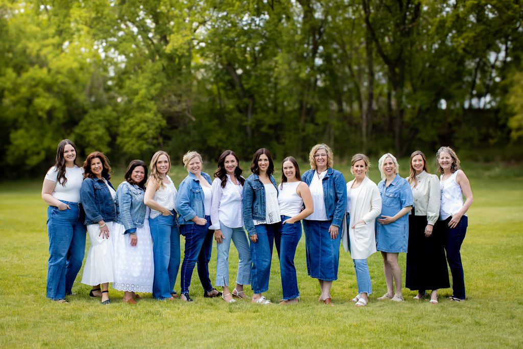Photo of a group of 13 smiling women standing next to each other in a line at an outdoor location.
