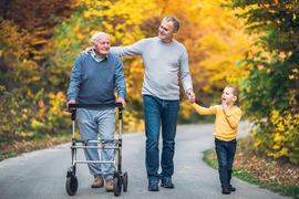 Grandpa with walker, dad and grandson walking on trail in fall colors
