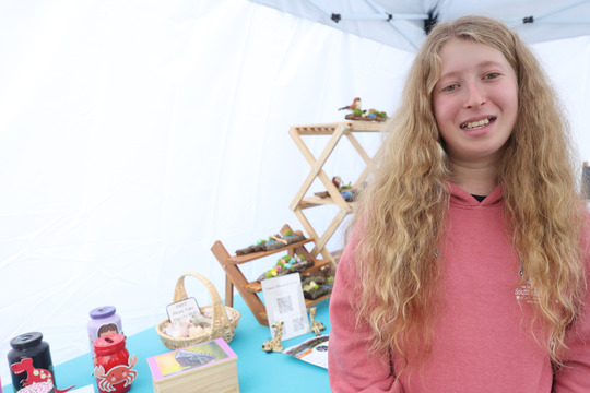 Photo of a young girl standing in front of a table with a colorful display of handmade goods.