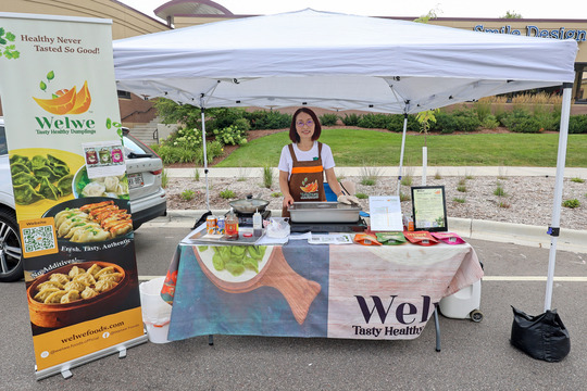 Photo of a woman standing behind a table with a pan of dumplings in front of her on the table