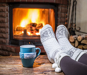 Person warming feed by an indoor fireplace, wearing socks with a mug nearby.