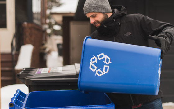Man putting items in a recycling cart outside during the winter