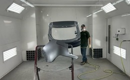 Auto body technician paints a car part in a spray booth 