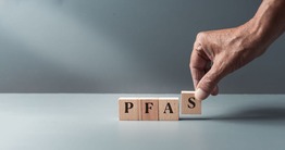 Hand placing wooden blocks on table with blocks spelling PFAS.