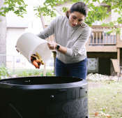 Woman dumping compost into outdoor compost bin in backyard