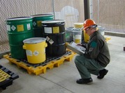 Person kneeling next to four 55-gallon metal drums