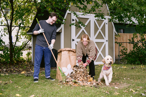 couple putting leaves in a yard waste bag with a dog sitting nearby
