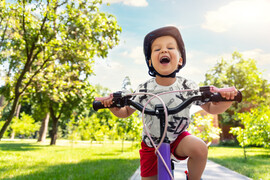Child riding a bike in a park, wearing a helmet, smiling.