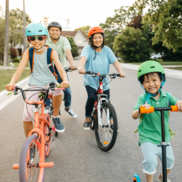 A family of bike riders, wearing helmets, biking on the street.
