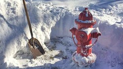 red fire hydrant that has had snow shoveled away from it with shovel resting against snowbank.