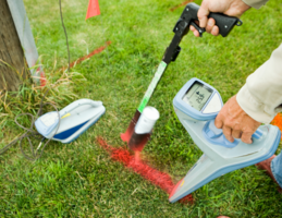 Medium close up of persons arm holding underground utility line locator in left hand and red spray paint in right hand