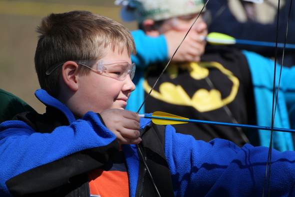 A  young boy aims a bow and arrow in a closeup shot