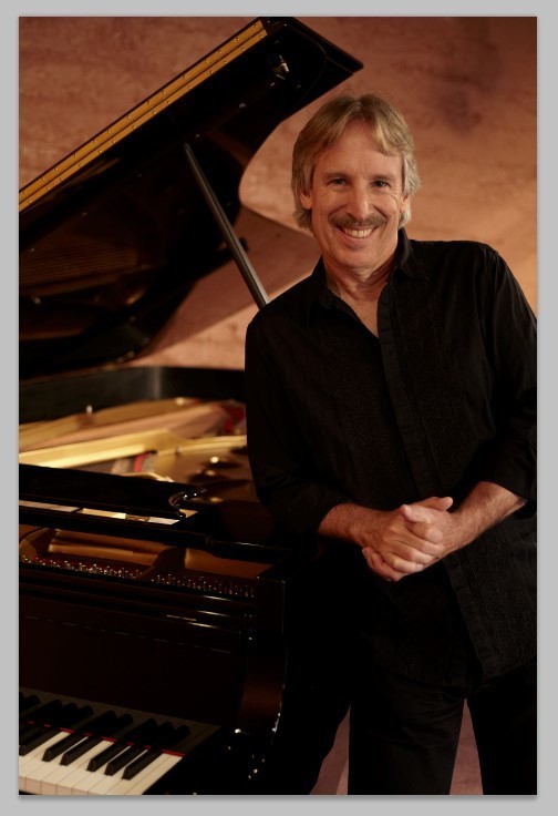 John Nilsen poses in front of a grand piano.