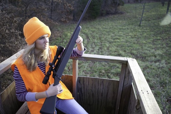 Woman holds a rifle in a deer stand.