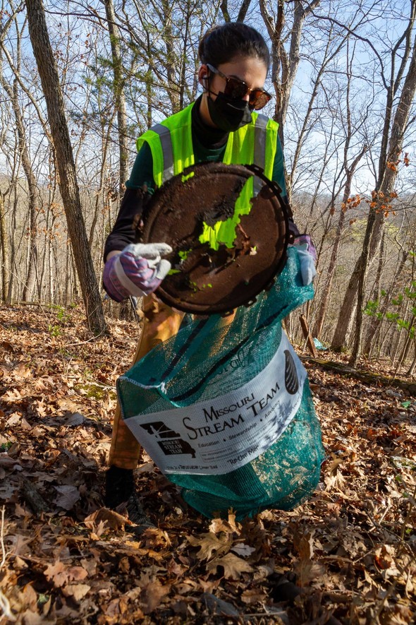 A woman puts a piece of metal garbage into a mesh trash bag.