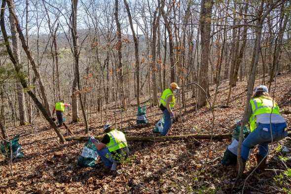A group of volunteers cleans up litter on the slope of a scenic ridge.