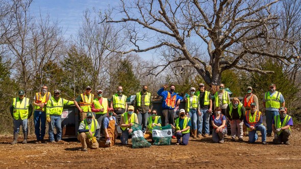 A large group of volunteer litter cleaners waering safety vests poses in front of a large dumbster.