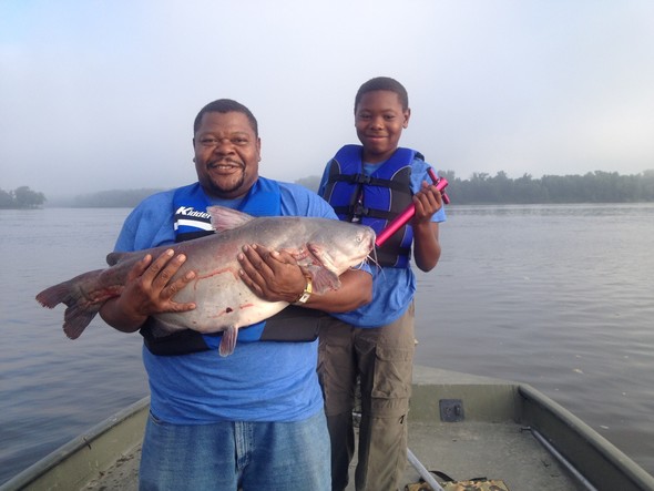 Father and son hold catfish on a boat