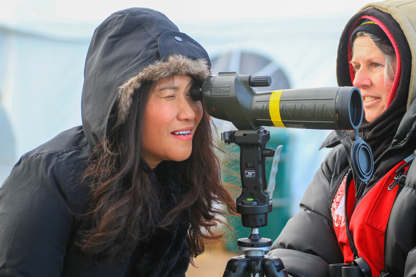 A woman looks through a spotting scope as a volunteer naturalist assists her.