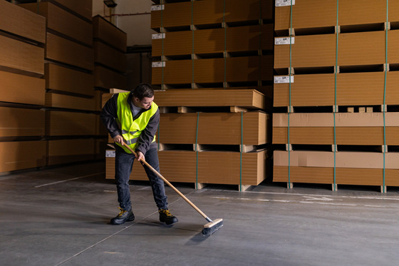 A man in a high visibility vest sweeping a warehouse with a push broom