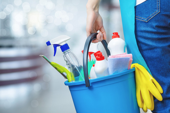 A person carries a bucket full of cleaning products.