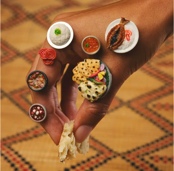 photo of a hand adorned with miniatures inspired by foods often eaten by hand around the world,
