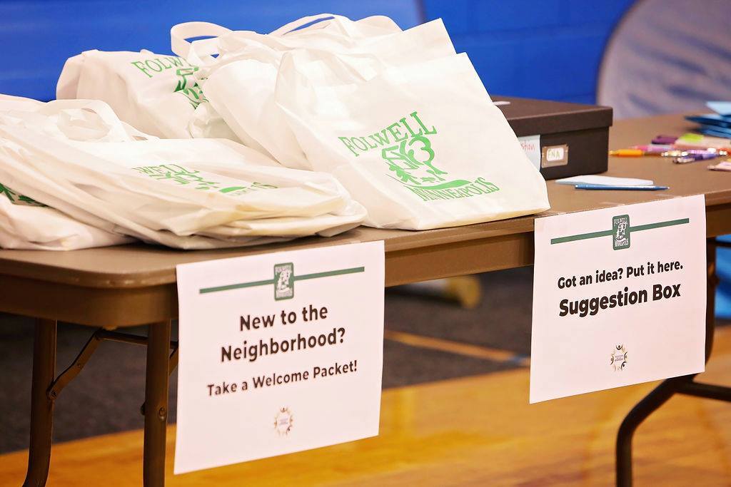 Folwell welcome bags with signs reading "New to the neighborhood? Take a welcome packet! Got an idea? Put it in the suggestion box."
