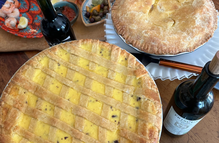 a picture of pies on a table accompanied by wine bottles and other appetizers