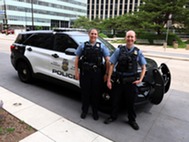 Two Minneapolis police officers smiling in front of their squad car.