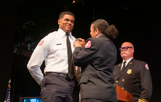An MFD cadet walks across the stage at the firefighter graduation ceremony.