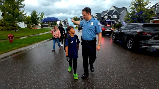 An officer walks with Ofc. Jamal Mitchell's children to the bus stop on their first day of school.